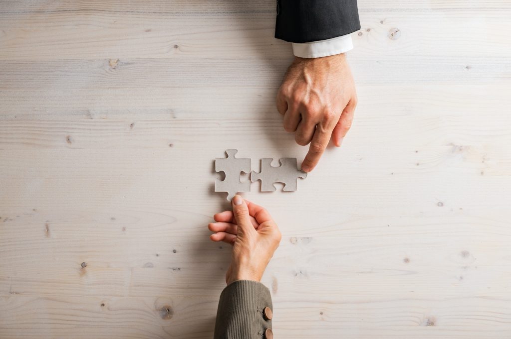 Male and female hand joining two blank matching puzzle pieces